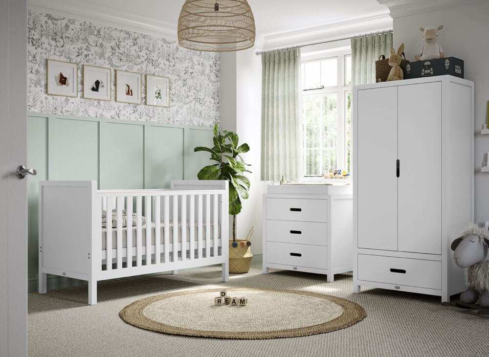 A white cot, changing station and wardrobe, dressed in bright nursery with statement wallpaper.