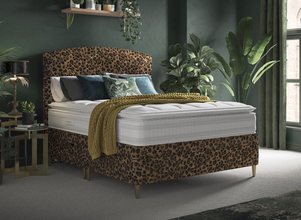 Leopard print headboard and divan base in a green bedroom with plants