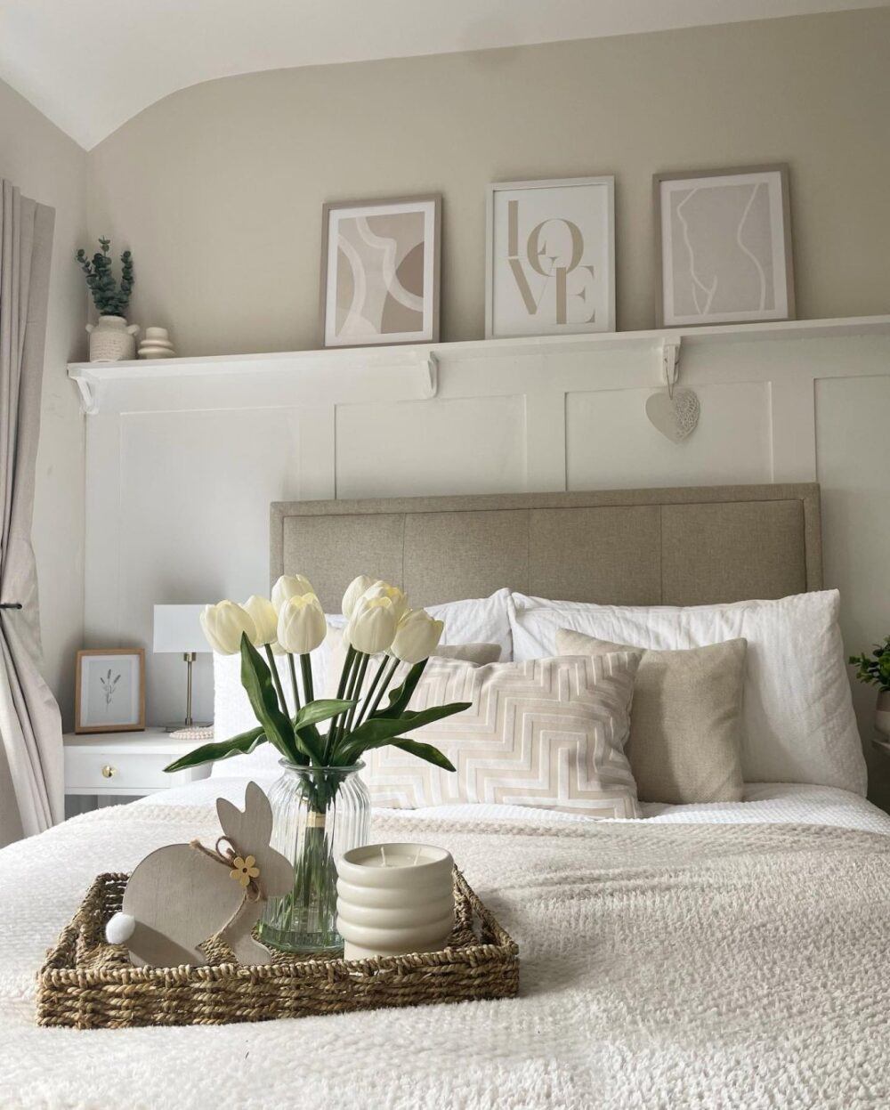 Beige upholstered bed, styled with neutral white sheets and flowers