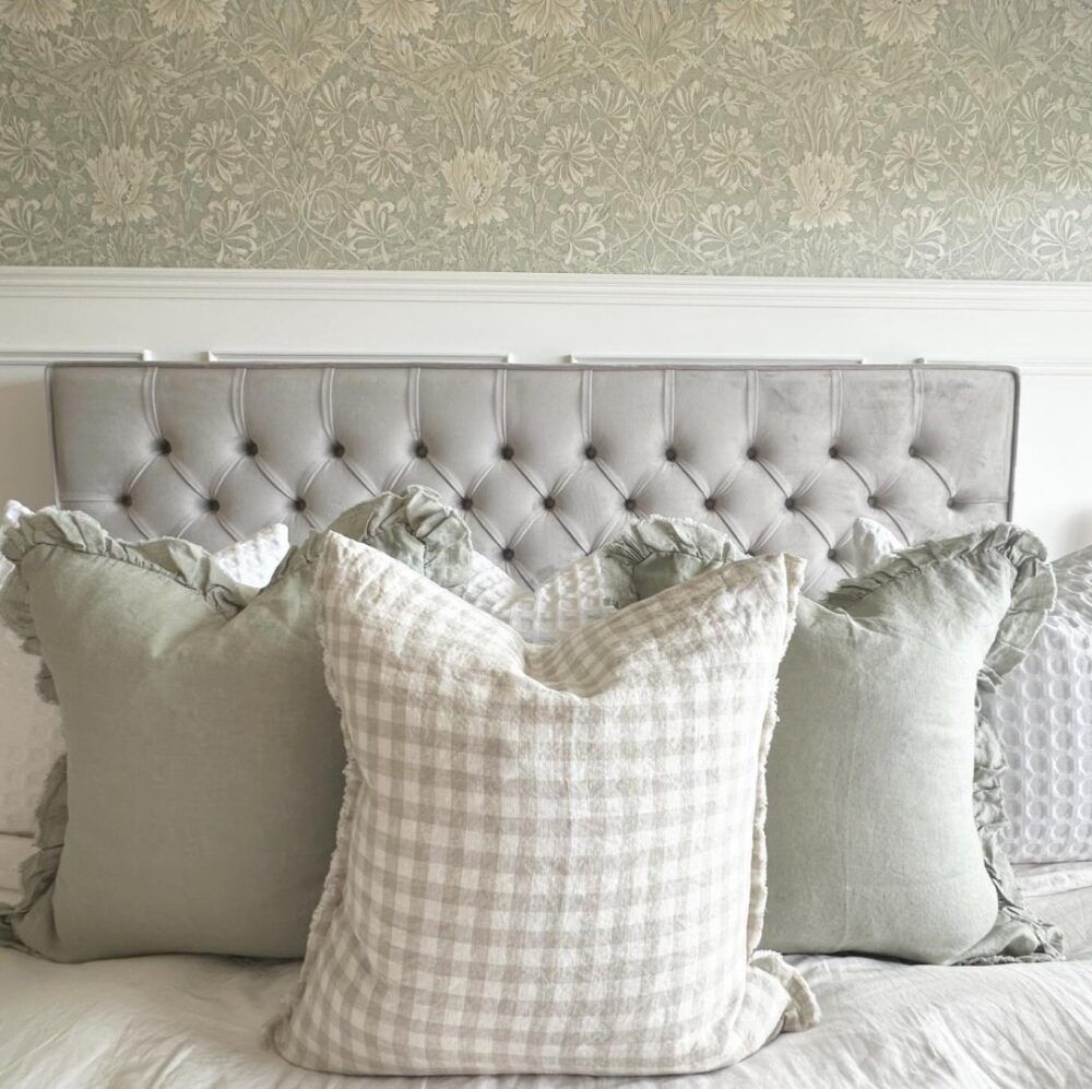 Grey detailed bed frame with large cushions and green patterned wallpaper