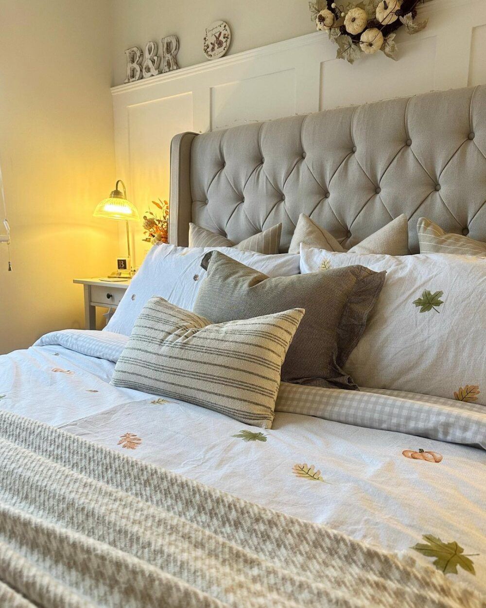 Beige buttoned bed, styled with neutral bed sheets with an autumnal leaf pattern