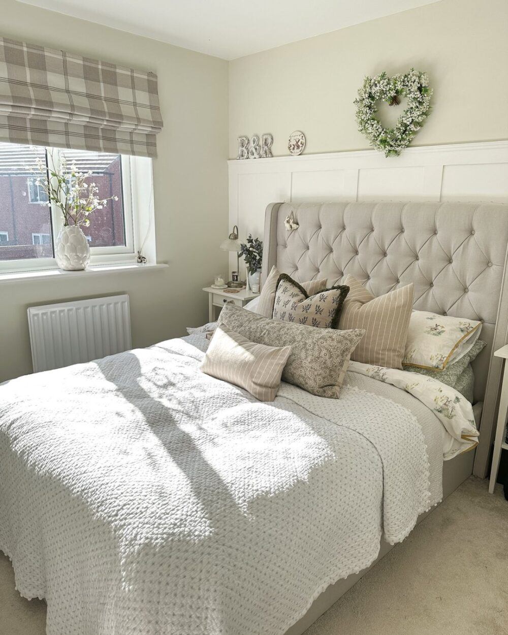 Beige buttoned bed, styled with neutral bed sheets with summer decorations including flowery heart wreath