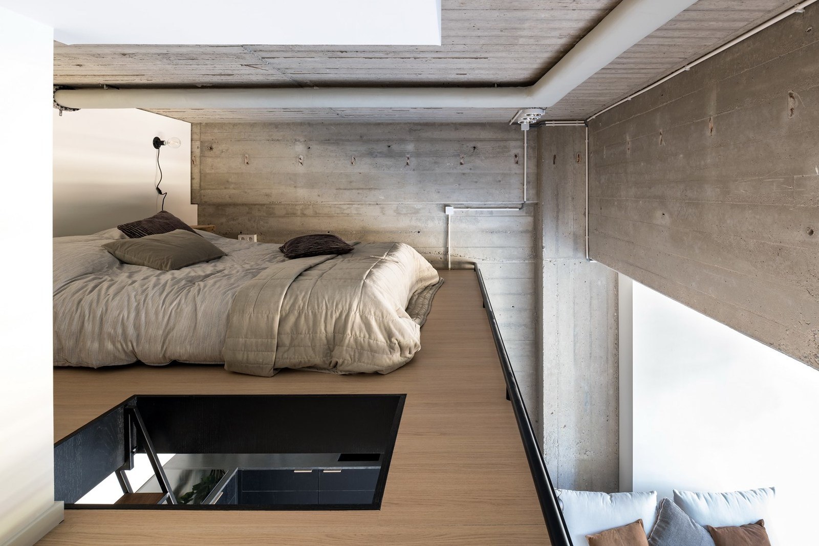 image of a mezzanine bedroom with a low bed frame and skylight in an industrial style home