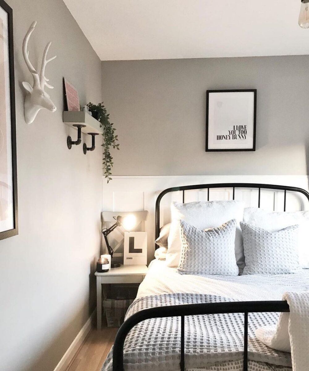 image of a black double metal bed frame with white bedding and cushions in a grey walled bedroom