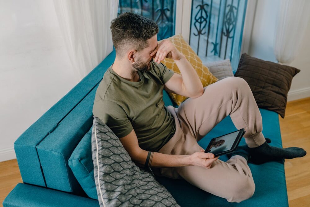 Man sitting on a blue sofa, looking visibly upset