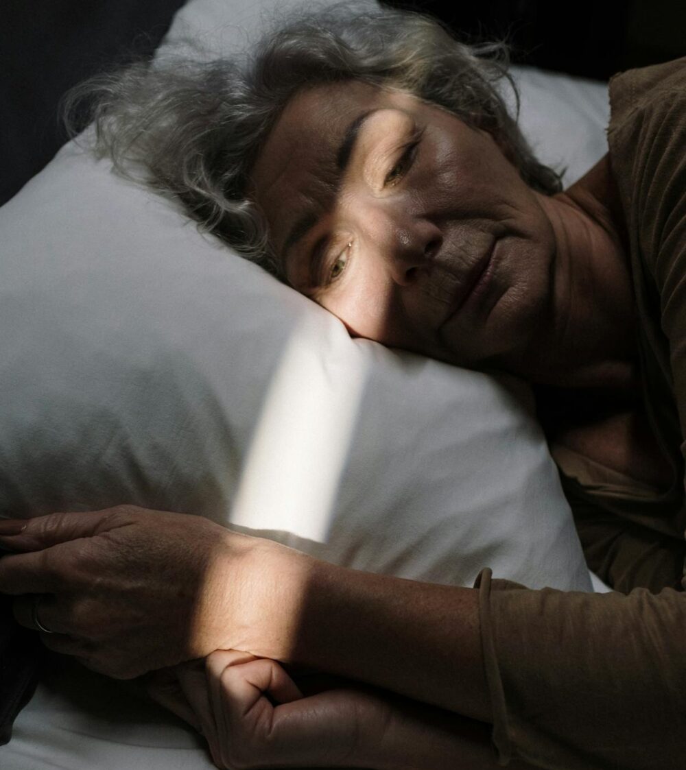 Older woman lying in bed with eyes open, light gently shining on her face