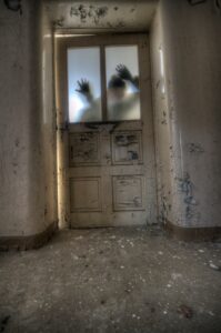 Spooky spectures push against the glass of a rotting door in a dilapidated house.