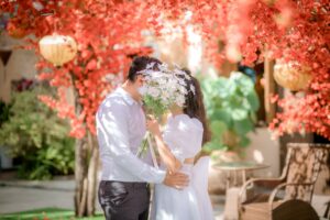 A couple have their first kiss at a wedding, surrounded by flowers. The kiss itself is obscured by a bouquet.