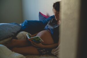 Pregnant woman in bed reading a child's book