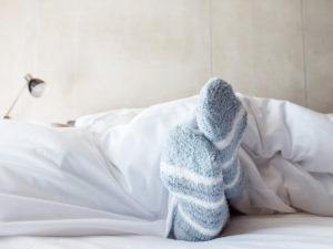 A person covered in a duvet, wearing powder blue and white striped socks in bed.