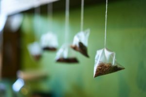 Tea bags suspended in the air in front of a blurred green wall