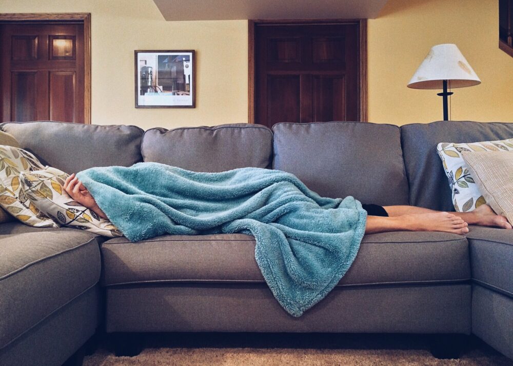 Sleeping on a grey sofa with a blue blanket overtop in the living room