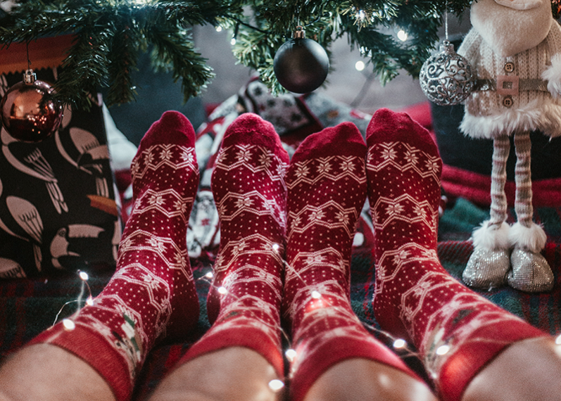 Two people with red festive socks on sit in front of a Christmas tree