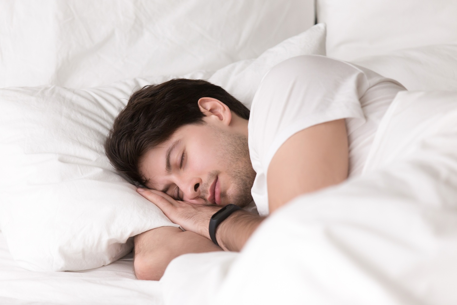 Young guy sleeping in bed wearing smartwatch or sleep tracker